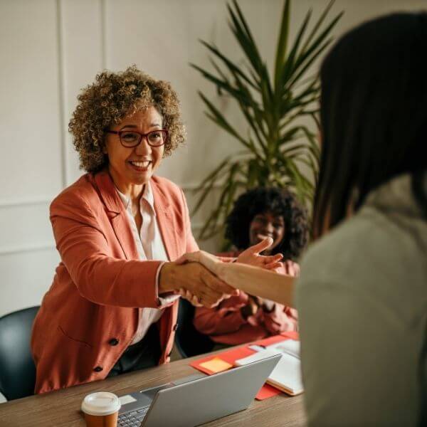 woman reaching over desk happily greeting a colleague woman reaching over desk happily greeting a colleague